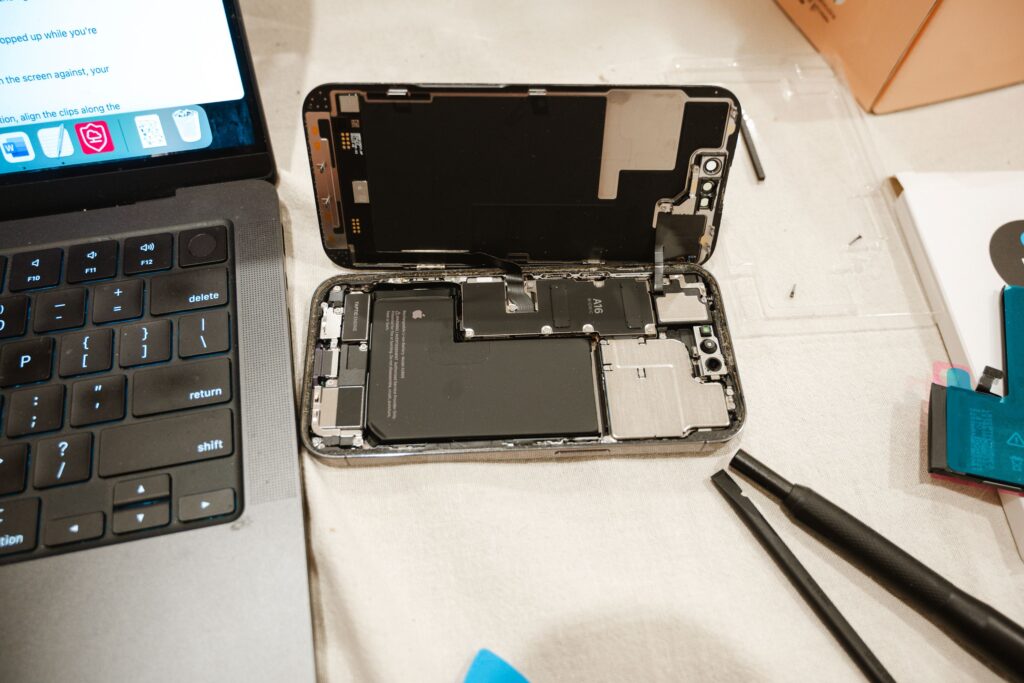 Open iPhone with repair tools and laptop, showcasing DIY battery replacement process.