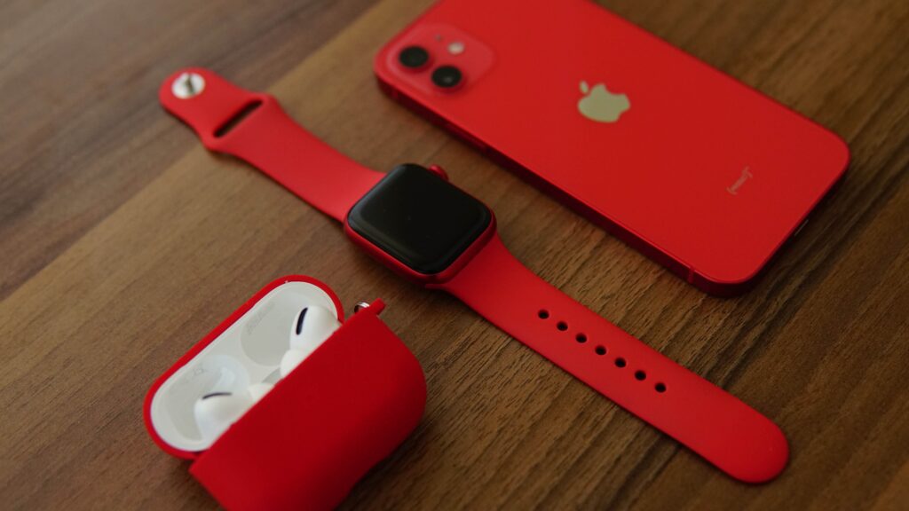 Red smartphone, smartwatch, and wireless earbuds on wooden table.